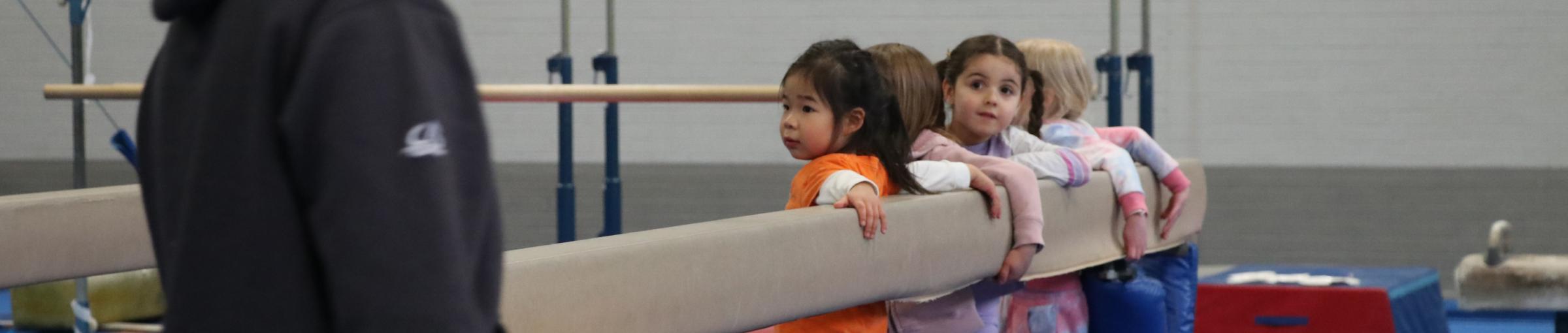 girls in gymnastics class holding on beam